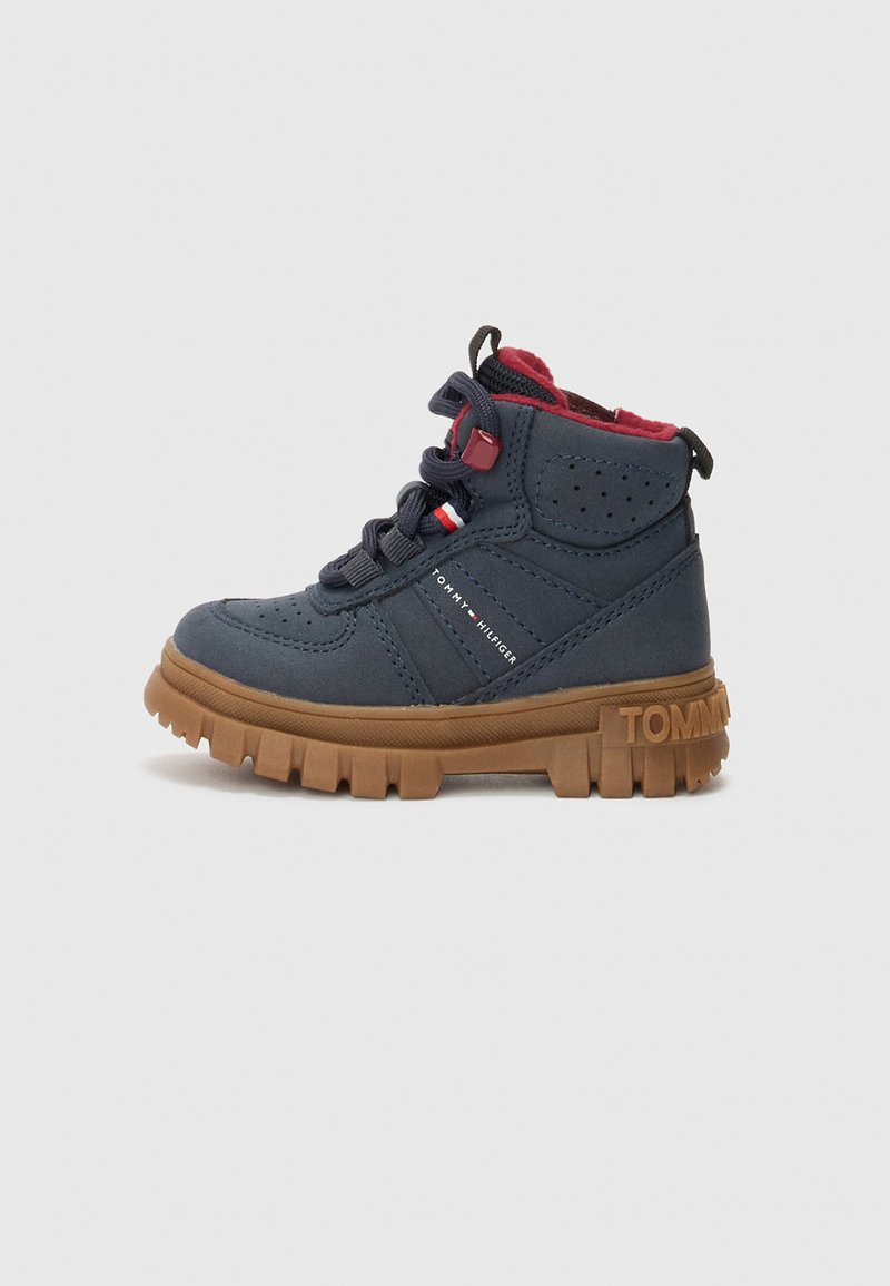 Botas sintéticas de media caña azules con suela de goma, acentos rojos y cierre de cordones. Presentan lados texturizados y detalle del logo en el talón.