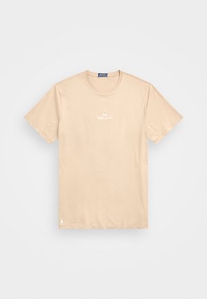 Beżowy T-shirt z krótkim rękawem i okrągłym dekoltem, z małym białym napisem "Polo Ralph Lauren" na piersi oraz logo w pobliżu dolnego brzegu.
