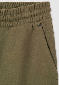 Oliwkowe dresy z rypsowym elastycznym pasem, z boczną kieszenią i teksturowanym materiałem. Minimalistyczny design z subtelnym elementem metalowym.