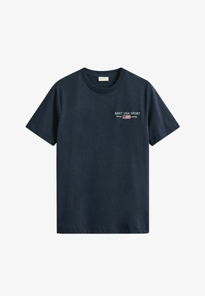 Tmavě modré tričko s krátkými rukávy, kulatým výstřihem a malým bílým nápisem "GANT USA SPORT" a emblémem americké vlajky na levé straně hrudi.