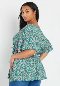 Blusa floreale con sfondo turchese, caratterizzata da maniche corte e una vestibilità ampia, adornata con piccoli fiori rosa, gialli e bianchi.