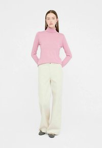 Roza pulover z visokim ovratnikom, oprijet zgoraj, v kombinaciji s kremasto širokimi hlačami. Mehka tkanina in preprost dizajn z minimalnimi okraski.