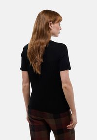 Haut noir côtelé à manches courtes avec une coupe ajustée. Le dos est simple, lisse, et présente un col rond. Associé à un pantalon à carreaux de ton sombre.