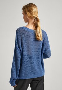 Zils adīts džemperis ar brīvu piegriezumu, kuram ir teksturēts raksts un ribotas piedurknes. Atvērta auduma struktūra piešķir elpojamību.