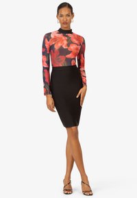 Bluse mit langen Ärmeln im floralen Design, kombiniert mit einem schwarzen Bodycon-Rock. Das Oberteil zeigt lebendige rote und pinke Blumen auf einem dunklen Hintergrund, hat eine enganliegende Passform und eine glatte Textur.