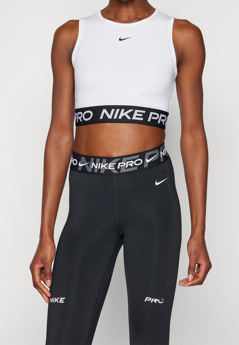 Biały sportowy krótki top z czarną gumą w pasie Nike Pro, zestawiony z czarnymi legginsami z logo Nike, wykonanymi z gładkiego, elastycznego materiału.