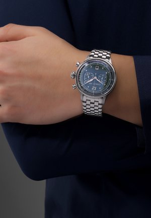 Reloj de acero inoxidable plateado con un dial azul, funciones de cronógrafo y display de fecha. Cuenta con una pulsera eslabonada y una caja redonda.
