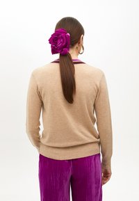 Beżowy sweter z fioletowym kołnierzykiem, w połączeniu z błyszczącymi, śliwkowymi spodniami plisowanymi. Włosy związane z tyłu dużym fioletowym kwiatem z materiału.