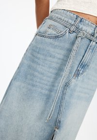 Világoskék denim szoknya húzózsinórral a derekán, oldalsó hasítékokkal és klasszikus öt zsebes dizájnnal, puha, megkopott textúrával.