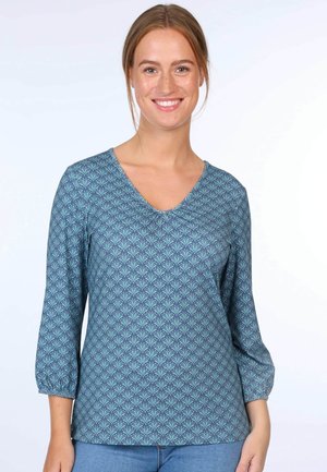 Dreiviertelärmel, V-Ausschnitt Oberteil in Teal mit einem geometrischen Muster, das blattähnliche Formen in dunklerem Blau zeigt. Weicher Stoff mit glatter Textur.