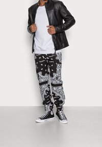 Chaqueta de cuero negra, sudadera gris y pantalones negros con patrón de bandana. Zapatillas altas negras con acentos de suela blanca.