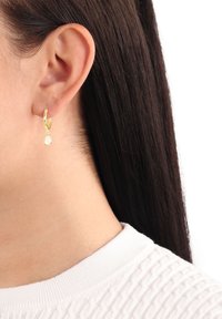 Goldene Ohrstecker mit einem tropfenförmigen Edelstein, der von der Basis hängt. Schlichte Gestaltung, polierte Oberfläche und leichtes Aussehen.