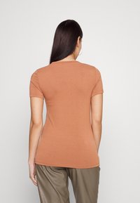 Krátký rukáv, přiléhavé tričko v barvě spáleného pomeranče, hladká bavlněná tkanina, kulatý výstřih, ploché švy, nošeno s měkkými, světlými kalhotami.