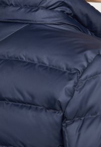 Sezione di giacca imbottita blu navy con texture trapuntata, caratterizzata da tessuto lucido, cuciture orizzontali e imbottitura prominente per isolamento.