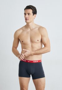Férfi Nike boxer alsónadrág sötétszürke színben, piros rugalmas derékpánttal, amelyen a Nike logó található. Simává anyag és testhezálló fazon.