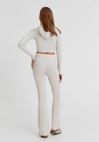 Hoodie cropped beige clair avec capuche, tissu texturé et ourlet festonné, associé à un pantalon évasé beige clair, également avec une finition texturée.