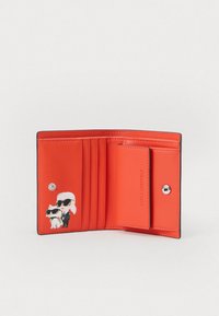 Czerwony skórzany portfel z wieloma miejscami na karty i zapięciem na zatrzask. Posiada ilustrację dwóch postaci w czarnych okularach przeciwsłonecznych.