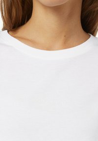 Witte katoenen t-shirt met een ronde hals en een subtiele reliëftekst "CASUAL IDENTITY" op de voorkant. Zachte textuur.