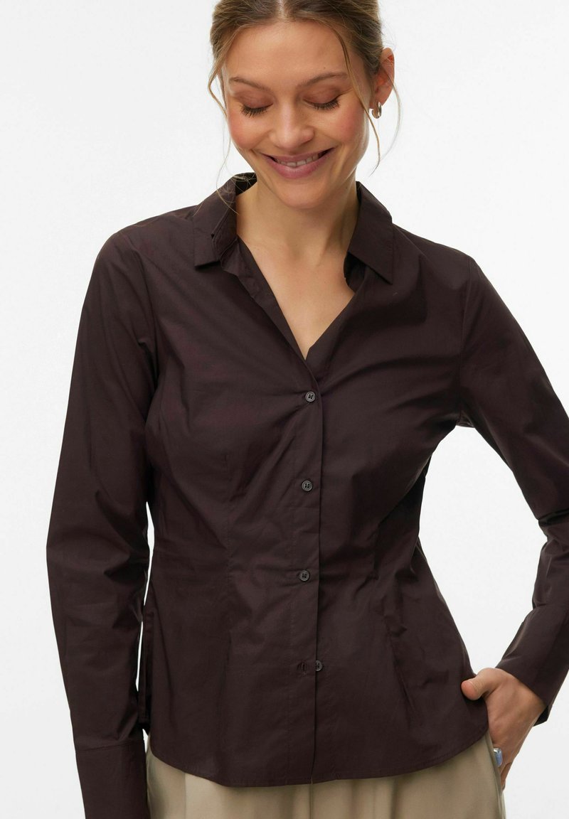 Chemise marron à manches longues avec col et boutons, au design ajusté et en tissu léger et lisse. Légèrement brillante, sans motifs visibles.