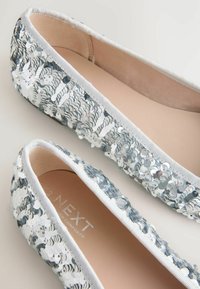 Ezüst-fehér színű, flitterrel díszített balerina lapos cipő, sima belső béléssel és lekerekített orr-résszel, finom peremmel.