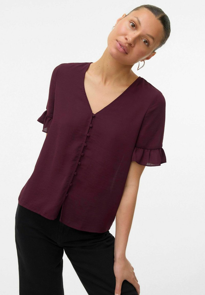 Bordeaux blouse met korte mouwen en een V-hals, voorzien van een knopenlijst aan de voorkant en ruches aan de mouwen, gemaakt van lichtgewicht stof.