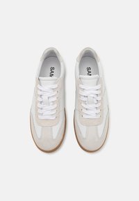 Sneakers bianchi e grigio chiaro realizzati con un mix di materiali in pelle e scamosciato, con lacci piatti bianchi e suola in gomma. Presentano cuciture decorative.