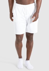 Weiße Baumwollshorts mit einem elastischen Bund und Kordelzug. Getragen mit weißen Knöchelsocken; glatte Textur und lässige Passform.