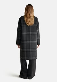 Cappotto lungo grigio a righe in lana con spalle scese e vestibilità rilassata. L'interno presenta foderatura in un colore uniforme.