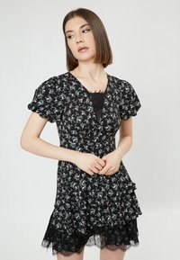 Vestido negro con flores, con mangas cortas abullonadas, escote en V, falda con volantes en capas y ribete de encaje en el dobladillo. Presenta pequeños patrones florales en rosa y verde.