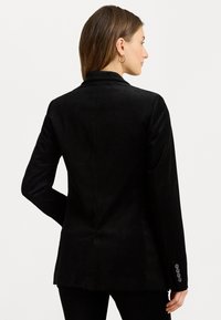 Čierny oblekový blazer s hladkou textúrou, s jedným rozventilovaným zadným dielom a gombíkovými manžetami. Navrhnutý pre priliehavý strih.