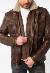 Braune Lederjacke mit mit Schaffell gefüttertem Kragen, Reißverschluss vorne und gestepfter Innenauskleidung. Verfügt über mehrere Vordertaschen und strukturierte Details.