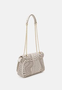 Beige handväska med logomönster, som har en strukturerad form, guldkedjeband och en slät lädertextur. Stängning högst upp.