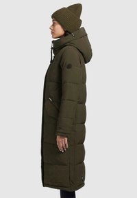 Oliven grøn pufferjakke med hætte, sidelommer og et logo patch på ærmet. Ribbede strikkede beanie i matchende farve.