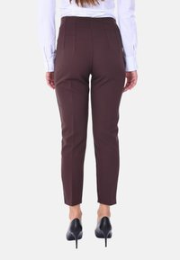 Pantaloni marroni attillati con una trama liscia, design a gamba affusolata e dettagli di cucitura visibili, abbinati a scarpe nere con tacco alto.