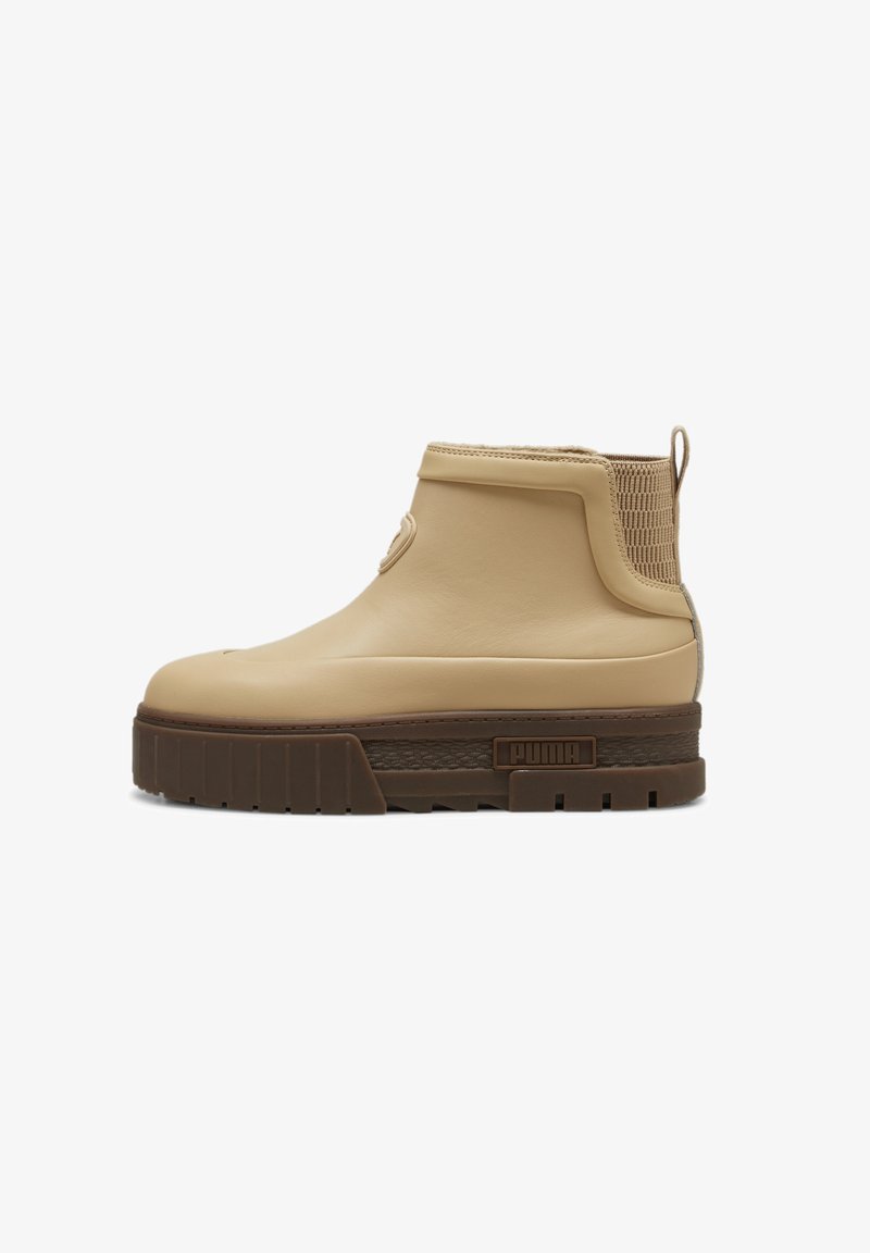 Bottes beige à la cheville avec une tige en cuir lisse, un panneau en maille texturée, une semelle épaisse marron, et un accent de marque sur le côté.