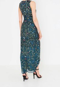 Long, sleeveless dress in dark teal with intricate floral embroidery in gold, red, and blue. Features a fitted bodice and sheer bottom.