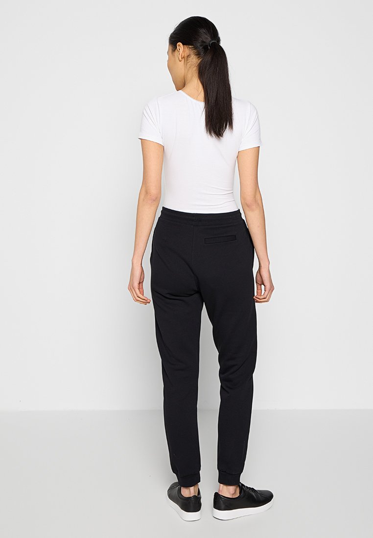 Pantalons de jogging noirs avec des poignets élastiques et une poche arrière, associés à une chemise blanche à manches courtes. Tissu lisse et coupe décontractée.