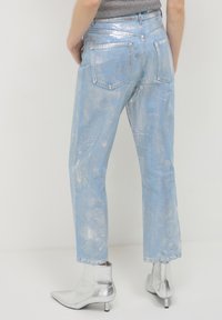 Jeans in denim azzurro chiaro con finitura metallizzata, taglio dritto, cinque tasche e dettagli logorati sottili. Abbinati a stivaletti argentati alla caviglia.