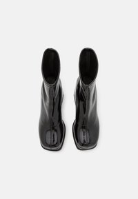 Zwarte laarzen van patenten leer met een slank ontwerp, vierkante neuzen en een glanzende, gladde textuur. Kenmerkend zijn de minimale stiksels.