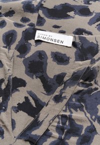 Tissu léger avec un fond beige et un motif léopard bleu foncé. Présente une étiquette indiquant "KAREN BY SIMONSEN."