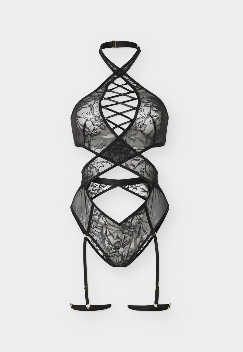 Body string en dentelle noire avec bretelles croisées, motifs floraux et porte-jarretelles intégrés, sur un fond clair uni.