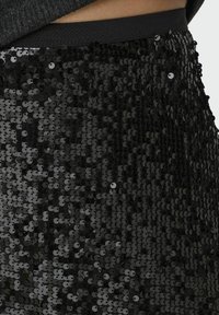 Gonna nera con paillettes, caratterizzata da una vestibilità aderente, una vita elasticizzata e una superficie lucida e strutturata creata da paillettes disposte in modo ravvicinato.