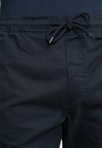 Bañador negro hecho de tela ligera, con cintura ajustable con cordón y diseño frontal plano con sutiles detalles de costura.