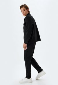 Sort to-delt outfit bestående af en skræddersyet jakke og slim-fit bukser, paired med hvide sneakers. Glat stof og minimalistisk design.