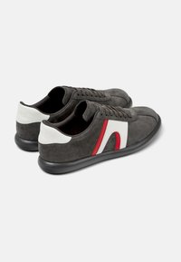 Grå mockasneakers med en vit och röd accentdesign, med rundad form, platt svart gummisula och traditionell snörning.