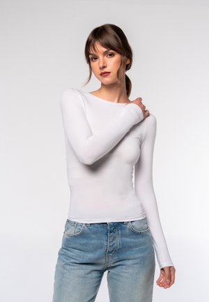 Long-sleeve white top with a fitted design and smooth texture. Paired with high-waisted light blue jeans. Minimalist style, no patterns.