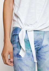 Top blanco y ligero con dobladillo anudado, combinado con leggings de teñido anudado en azul y verde que presentan un acabado suave y un diseño ajustado.