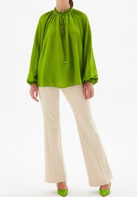 Blusa verde a maniche lunghe con scollo arricciato e dettagli con fiocco. Abbinata a pantaloni cream svasati e decolleté verdi brillanti.