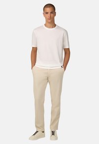 Biely krátky rukáv bavlnené tričko skombinované s béžovými nohavicami, ktoré sú vo voľnom strihu a štíhlom strihu. Model má na sebe biele tenisky.