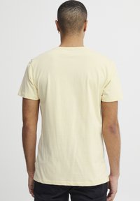 Gul kortermet T-skjorte laget av myk bomull. Har rund hals og rett kant med et enkelt, ubetydelig design.